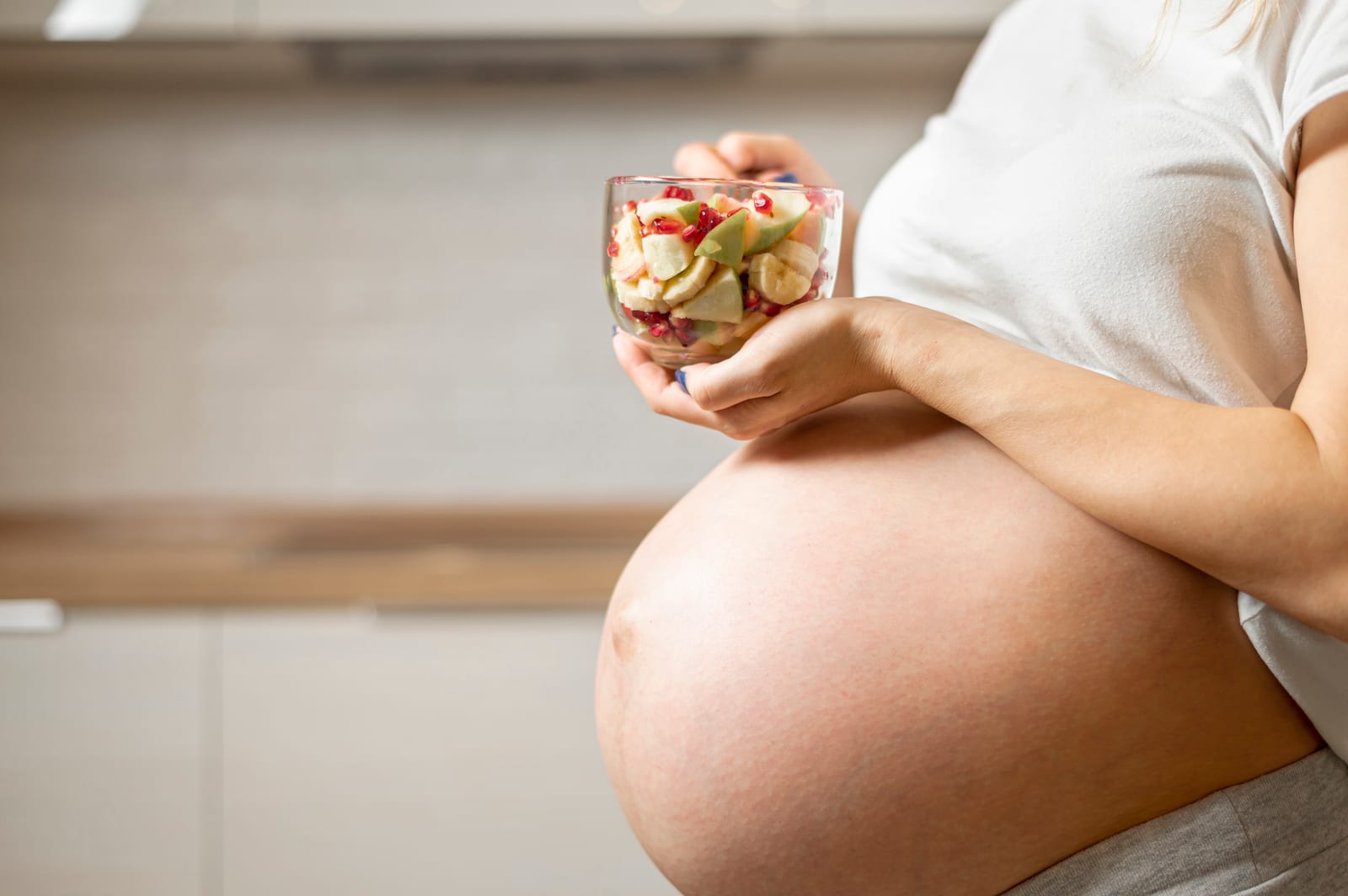 Pregnant woman holding a bowl of fresh fruit in the kitchen, nutrition and fertility
