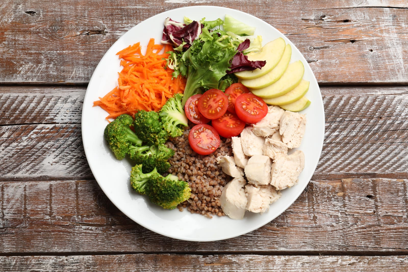 Balanced plate with chicken, broccoli, vegetables and fruit on a wooden table