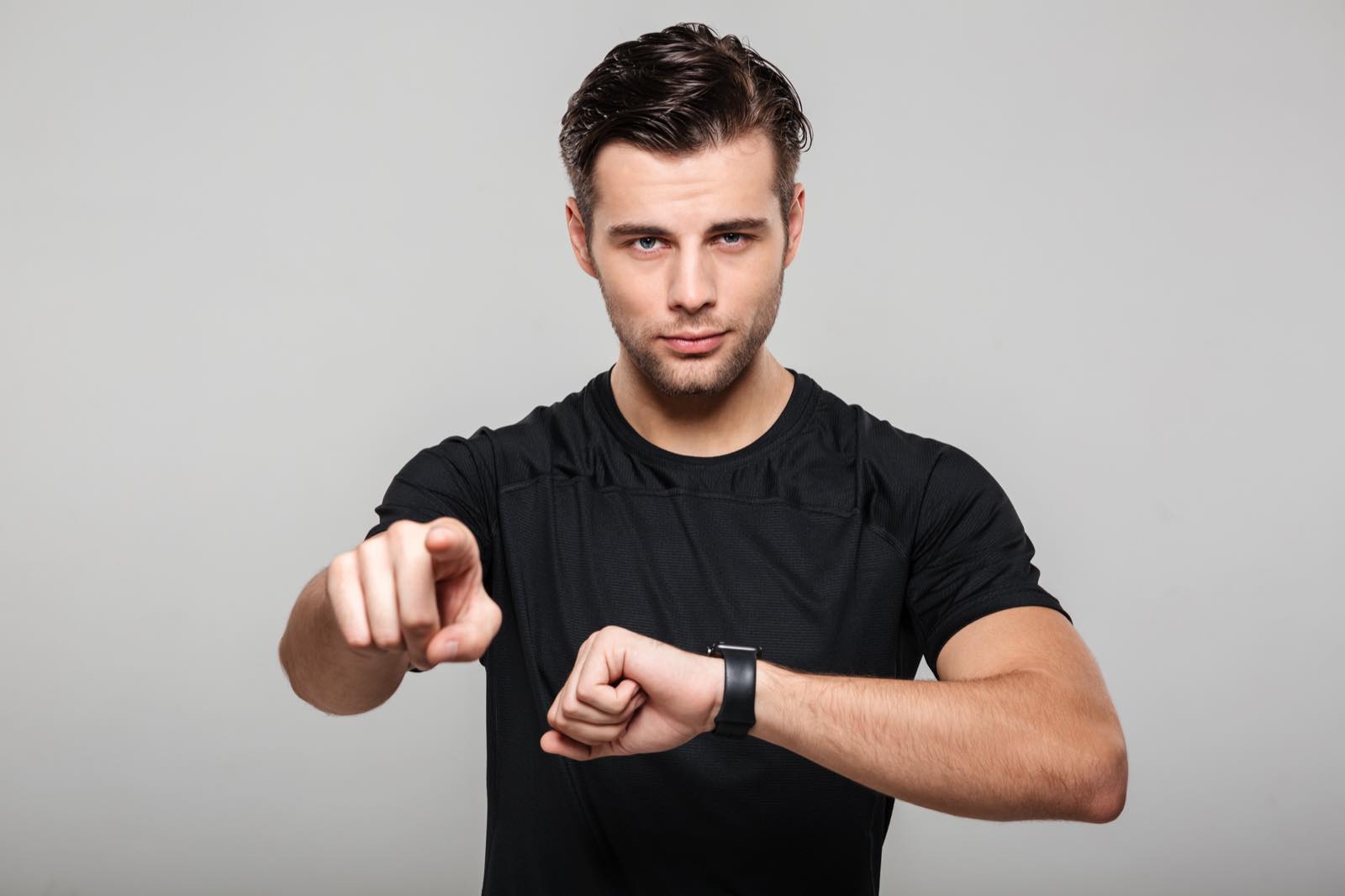 Hombre joven señalando hacia el frente mientras mira su reloj de pulsera