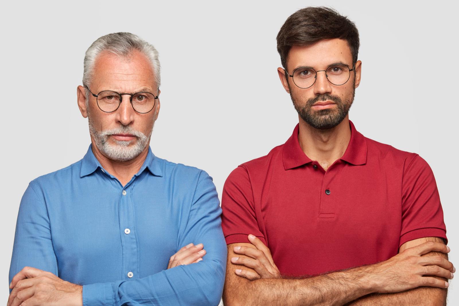 Hombre mayor y hombre joven de pie, uno junto al otro, con los brazos cruzados