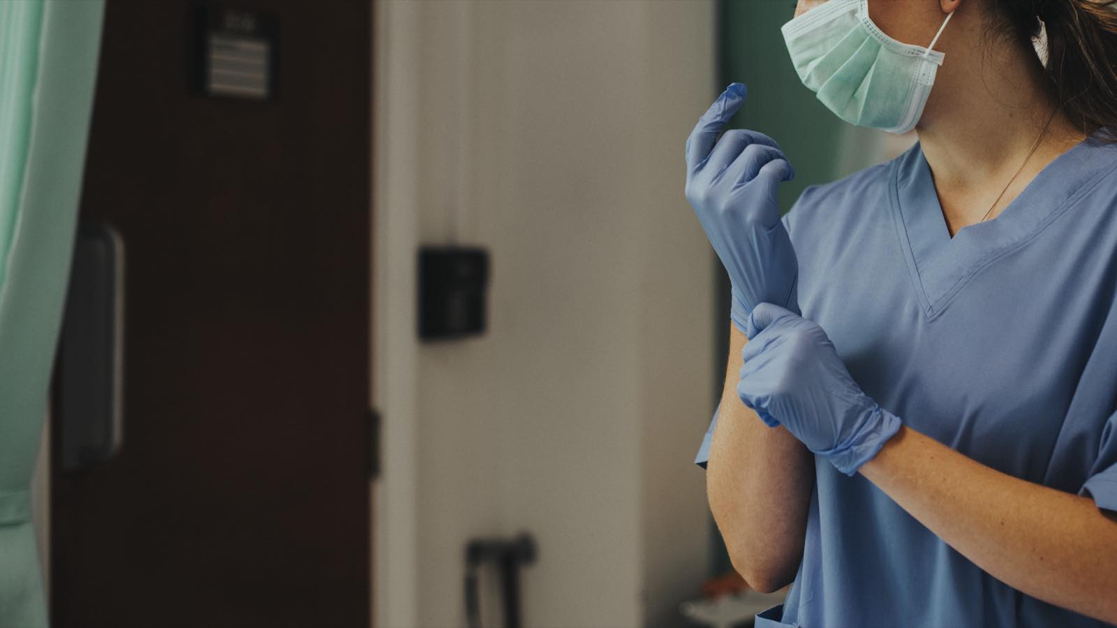 Enfermera con cubrebocas y uniforme azul ajustándose los guantes antes de un procedimiento