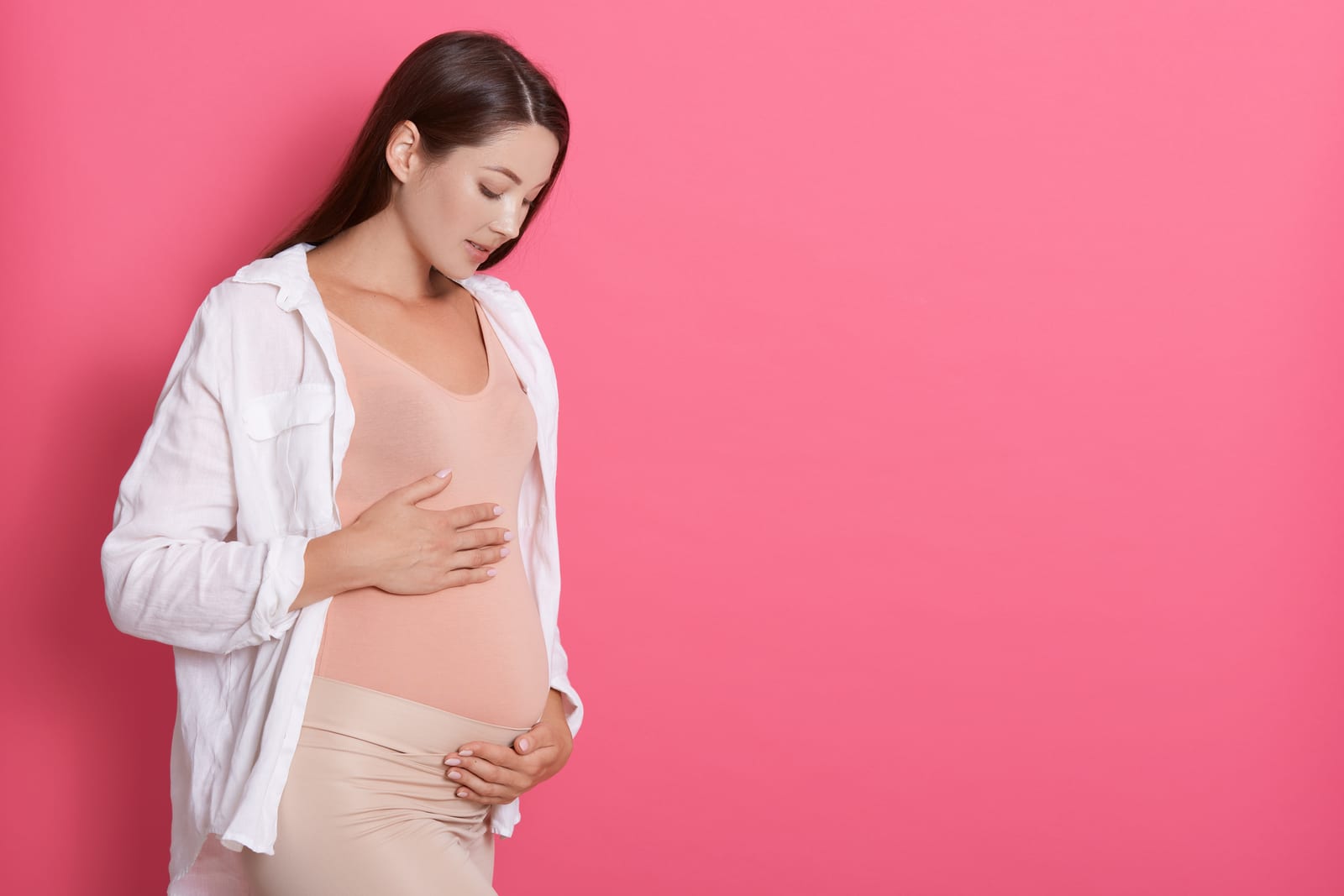 Pregnant woman tenderly looking at her belly against a pink background
