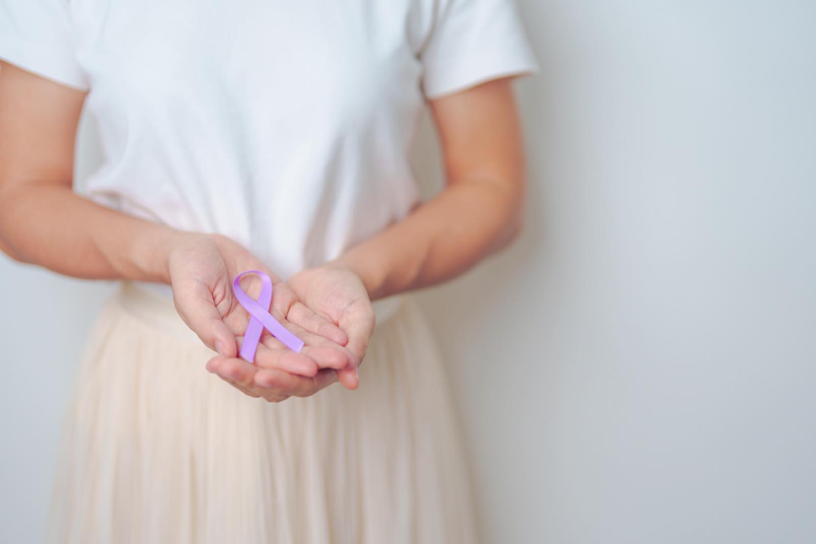 Mujer sosteniendo un listón lila de concientización sobre el cáncer entre sus manos