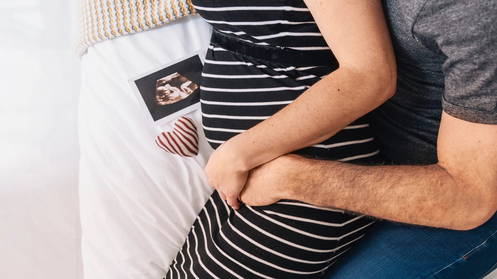 Couple embracing next to an ultrasound photo and a fabric heart on the bed