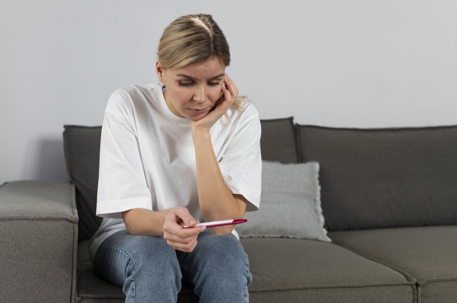Woman sitting on a couch looking worriedly at a pregnancy test