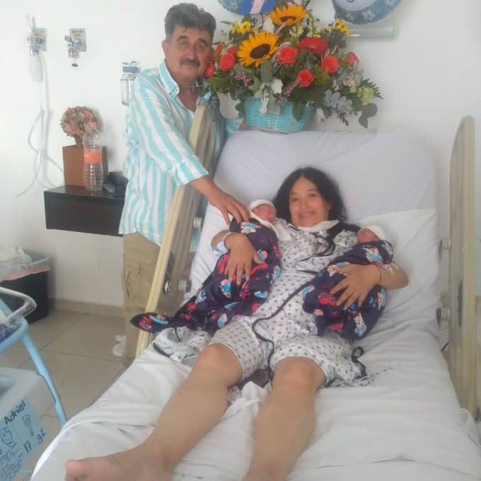 mujer mayor de 50 años junto a su esposo cargando bebés concebidos vía fecundación in vitro