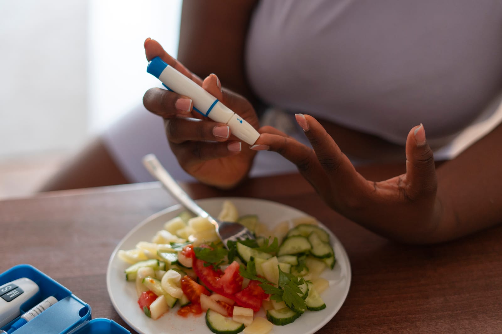 Woman checking her blood glucose next to a salad plate, insulin resistance and fertility