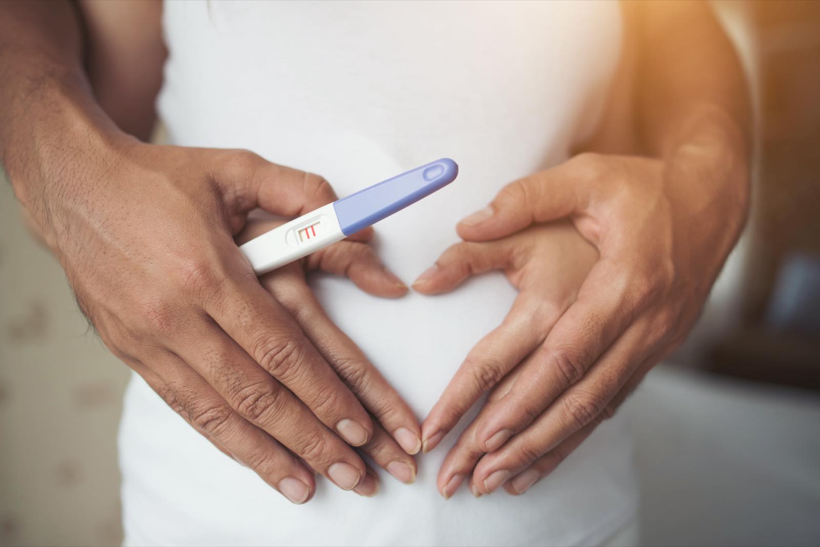Hands forming a heart over the belly while holding a pregnancy test