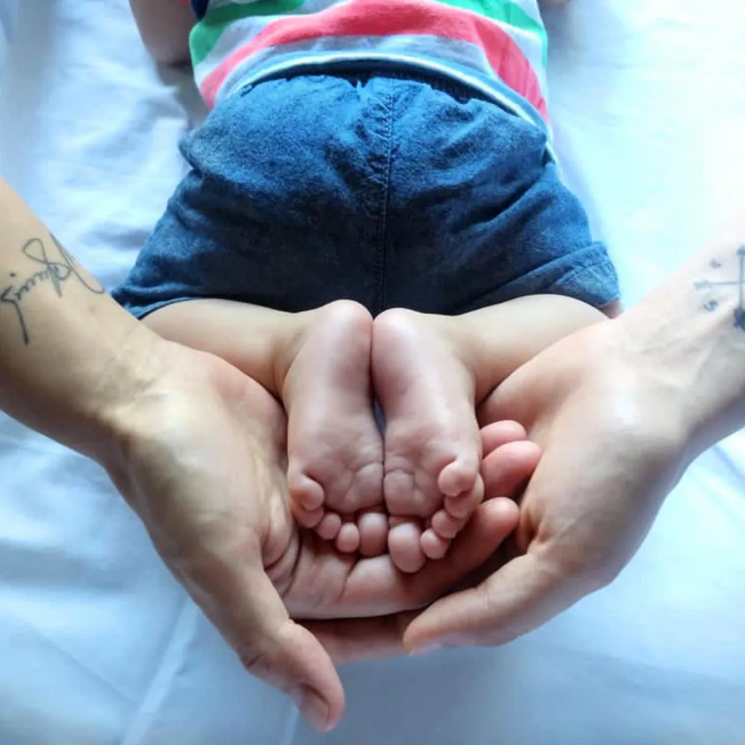Manos de las dos mamás sosteniendo los pies de su bebé