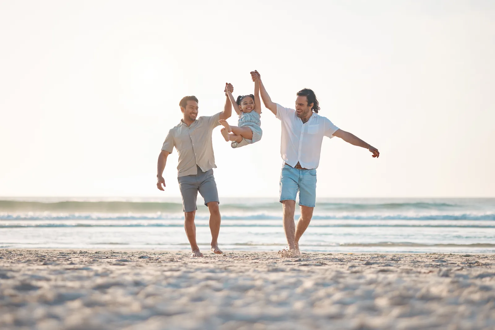 Pareja de hombres caminando por la playa con su hija