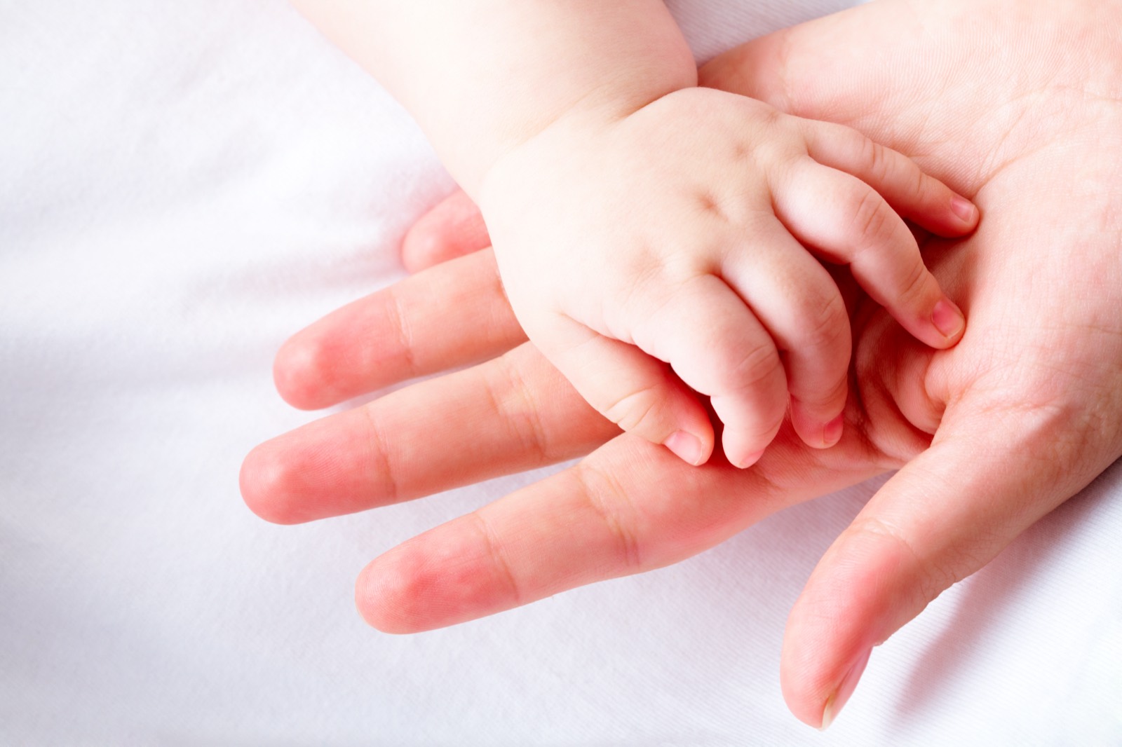 A baby's hand resting on a parent's hand, the goal of the Multicycle Programs: bringing your baby home